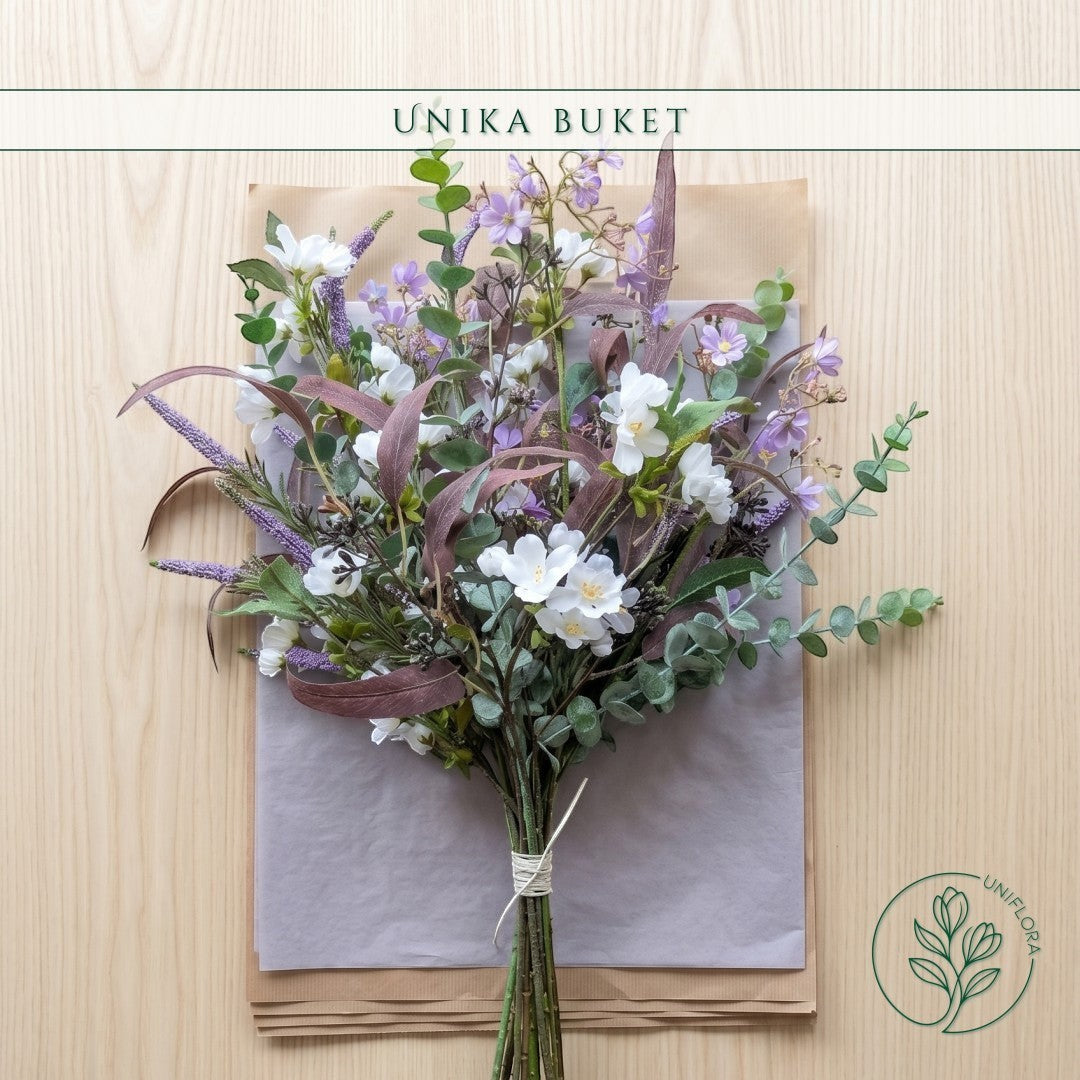 Uniflora buket Sensommerens Eng med vilde hvide og lilla blomster samt mørke bordeaux eukalyptusblade på lyst træ.