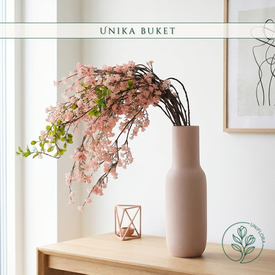 Uniflora Unika 26.60 buket med overhængende grene, lyserøde kirsebærblomster og grønne blade i en mat rosa vase.
